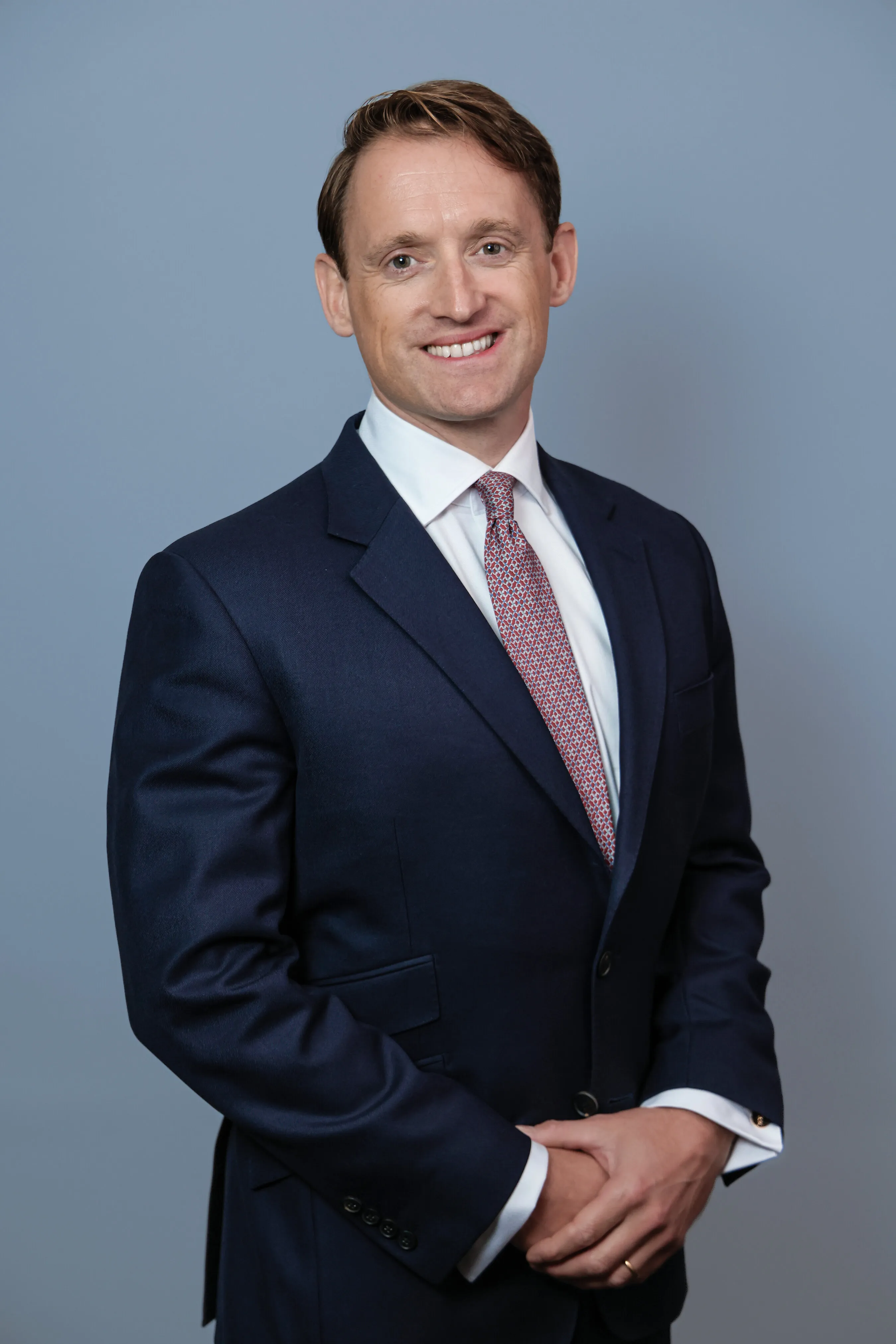 Burton Morgan Daniel in a navy suit and patterned tie against a gray background.