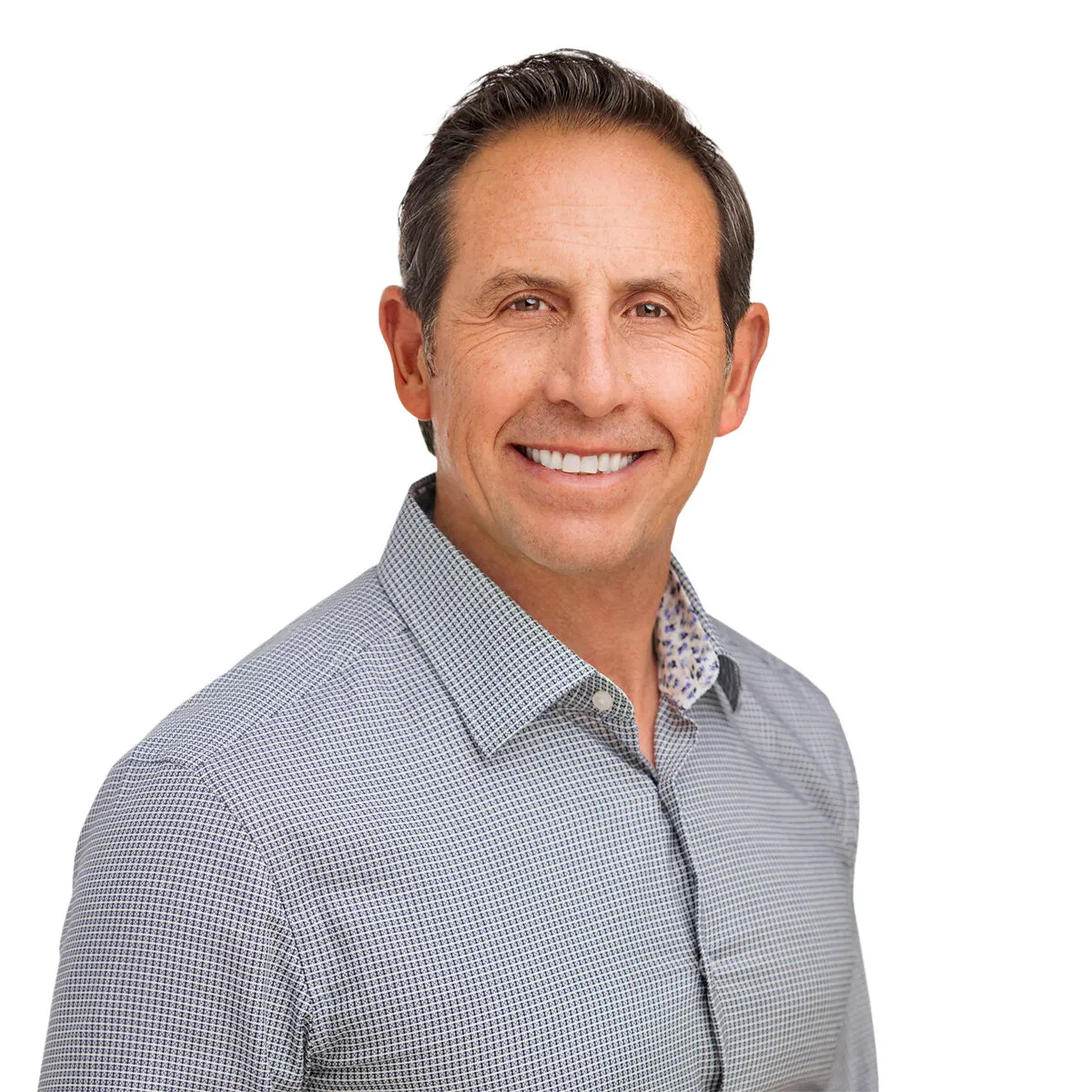Carlos Crabtree smiling in a patterned button-down shirt against a white background.