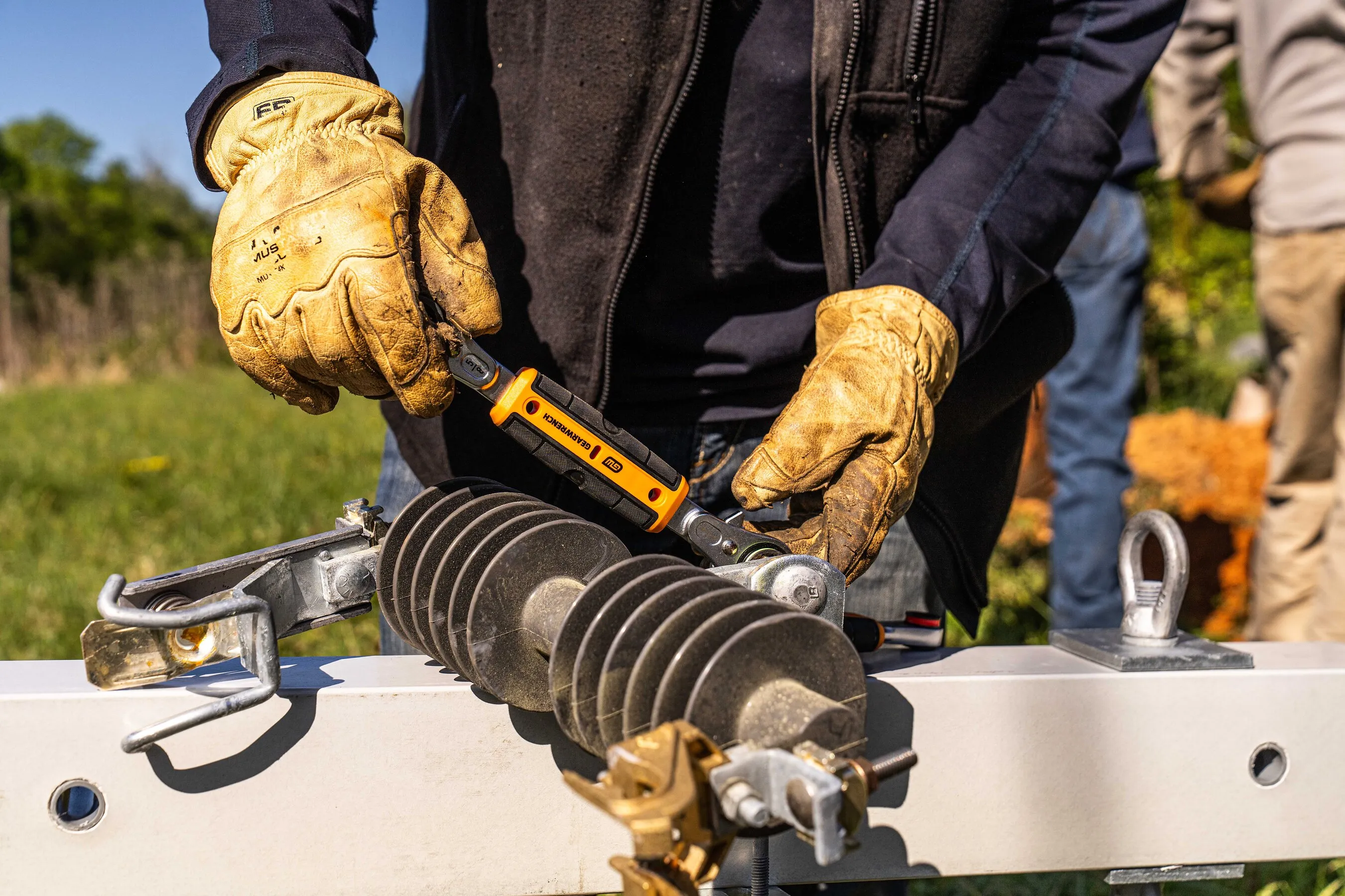 Gloved hands use a GEARWRENCH tool to service electrical equipment outdoors.