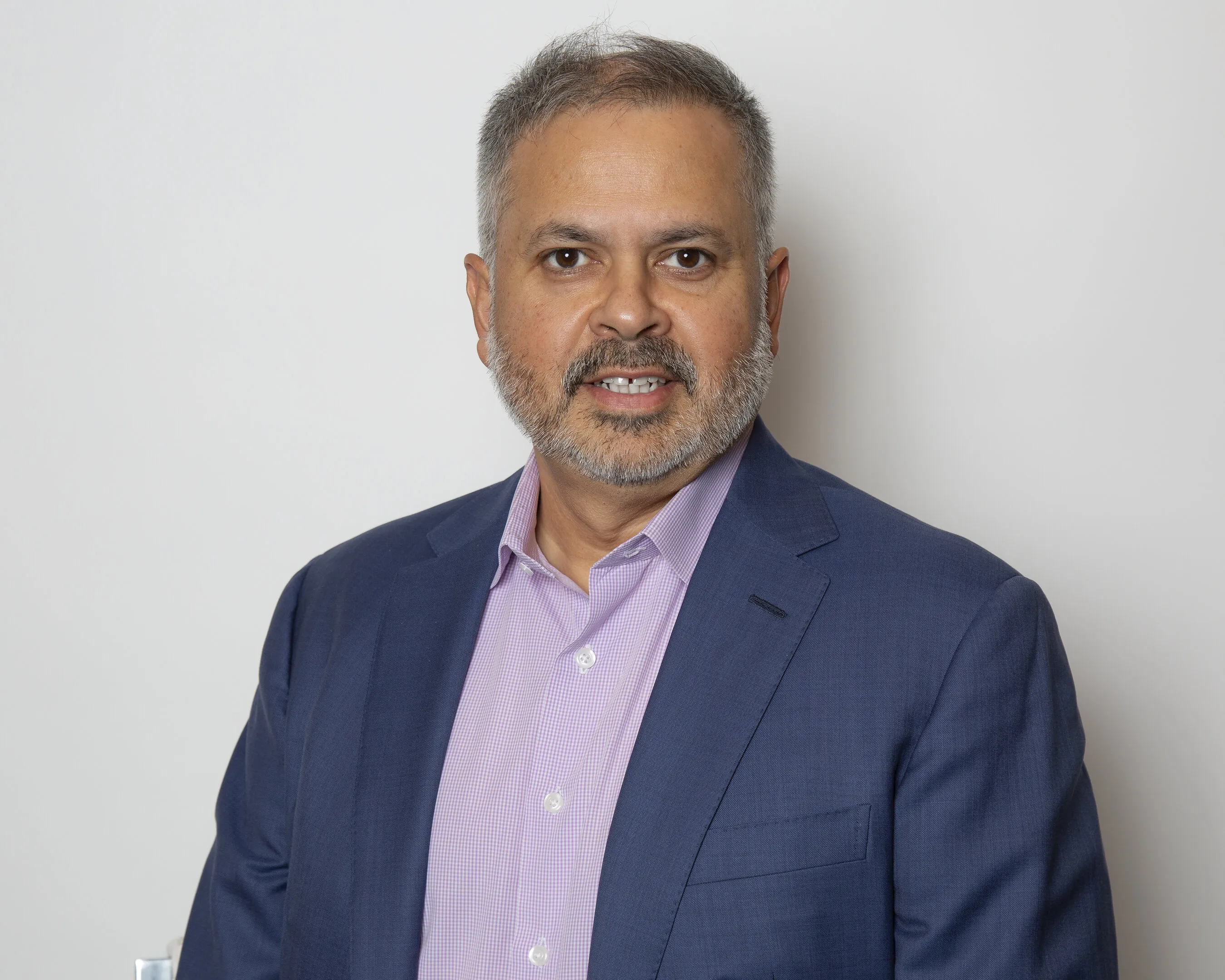 A person in a navy suit and pink shirt against a light background.