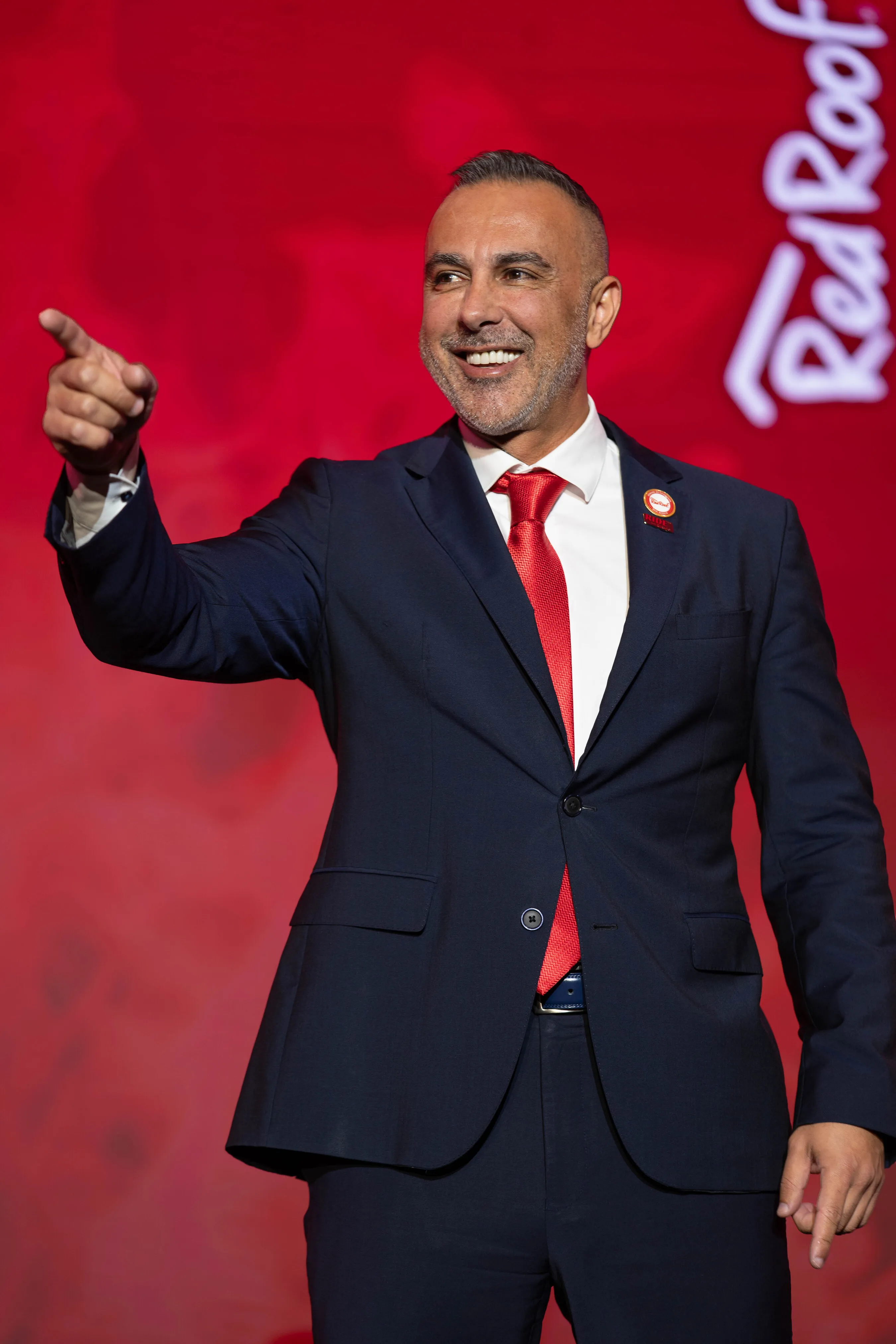 Red Roof President Zack Gharib points while standing in front of a red Red Roof backdrop.
